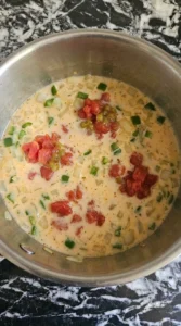 Creamy tomato and chile base forming in a saucepan for Cheesy Queso Dip.