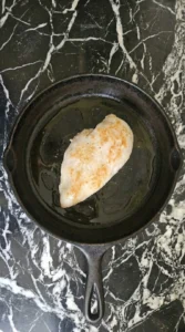 chicken breast cooking in skillet with golden crust forming