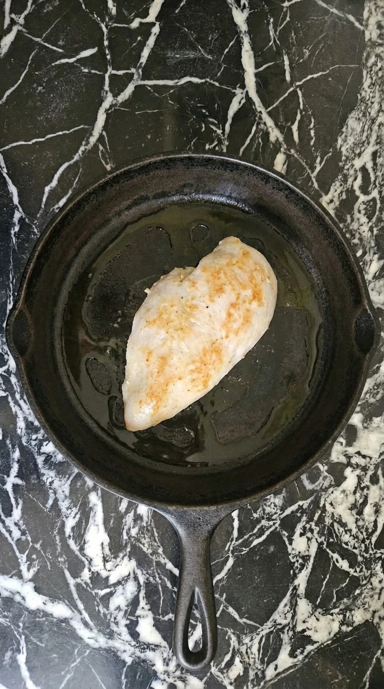 chicken breast cooking in skillet with golden crust forming