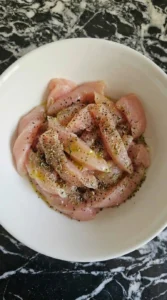 Seasoned raw chicken strips in a white bowl for Alfredo pasta