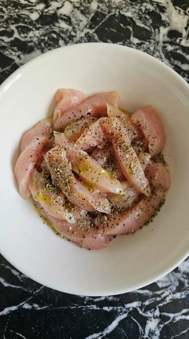 Seasoned raw chicken strips in a white bowl for Alfredo pasta