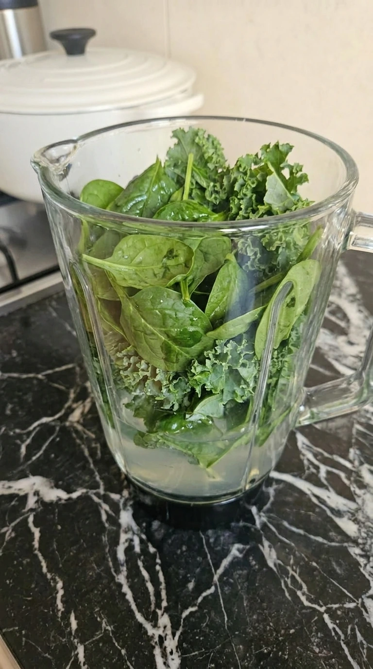 Baby spinach and curly kale layered with coconut water in blender jar
