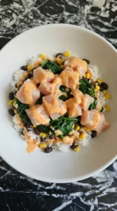 Coated chicken added over rice and bean base in a bowl