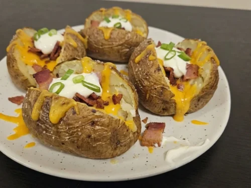 Loaded Baked Potatoes on a speckled white plate with melted cheddar, bacon, sour cream, and green onions