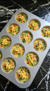 Muffin cups filled with egg mixture vegetables and cheese before cooking