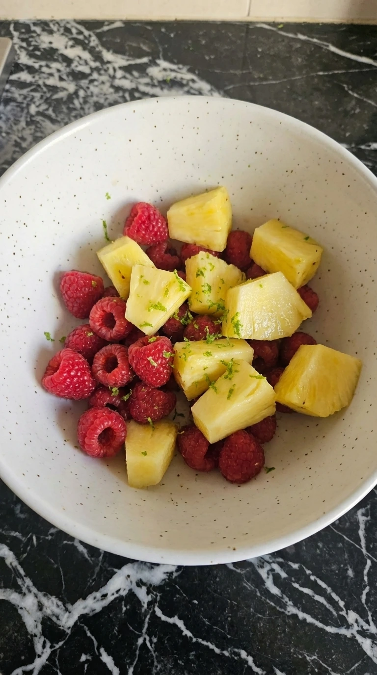 Raspberries and pineapple in a bowl with lime zest