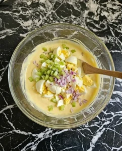 Chopped eggs and celery being folded into the creamy dressing