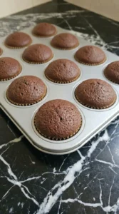 Freshly baked dark chocolate cupcakes with rounded domes cooling inside the aluminum tin