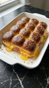 Baked mini sliders with deep golden tops and bubbling cheese in a baking dish