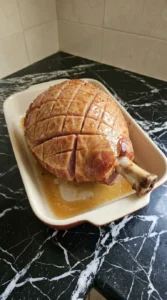 A spiral ham roasting in a ceramic dish with honey glaze.