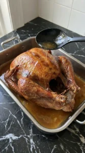 Pouring pan juices over a mahogany roast turkey