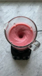 Pink fruit mixture blending inside a high-speed blender jar.