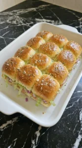 Brushing melted herbal garlic butter glaze onto the tops of mini sliders