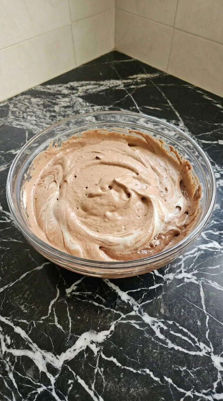 Light brown chocolate mousse mixture combined with whipped topping in a glass bowl.