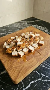 Diced grilled chicken breast pieces on a wooden cutting board showing a juicy white interior and seared crust