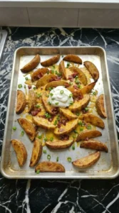Finished loaded fries on a sheet pan topped with melted cheese, bacon, a dollop of sour cream, and fresh chives