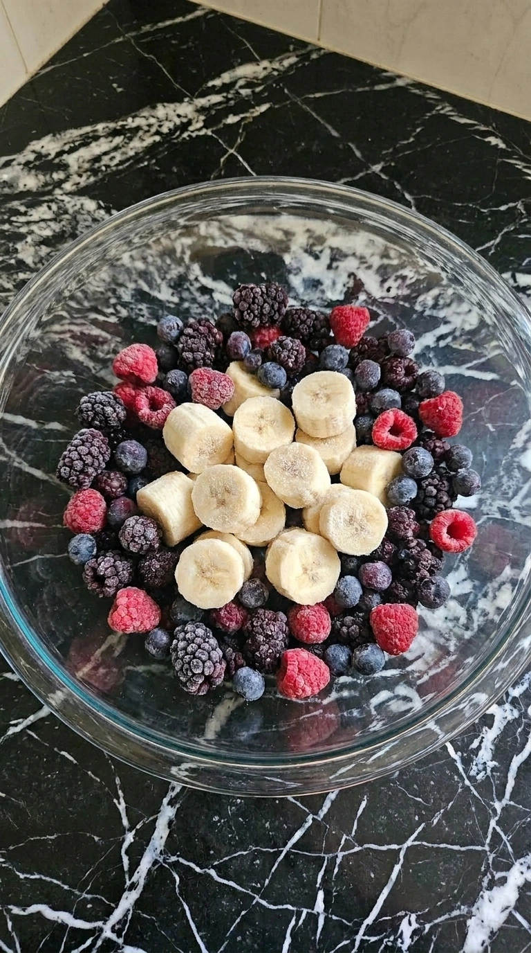 Frozen banana slices and mixed berries in a glass bowl