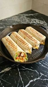 Toasted chicken wraps cooking in a cast iron grill pan showing golden brown surfaces and char marks