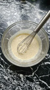 Creamy Caesar dressing being mixed with a whisk in a glass bowl