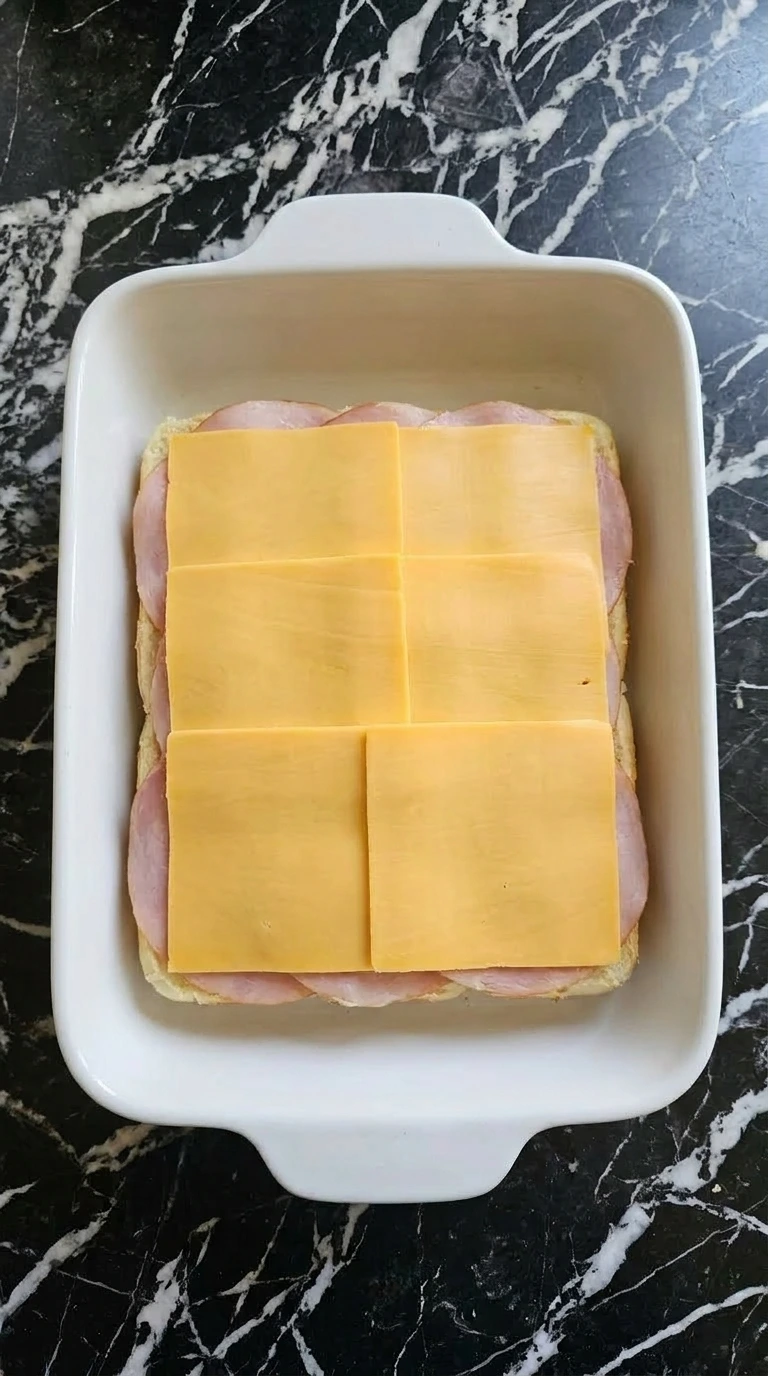 Layering deli ham and sharp cheddar cheese slices on top of slider buns