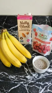 Almond milk, banana slices, and frozen strawberries layered inside a transparent blender jar.