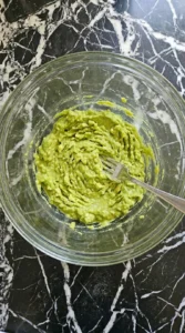 Mashing ripe avocados in a glass bowl with a fork