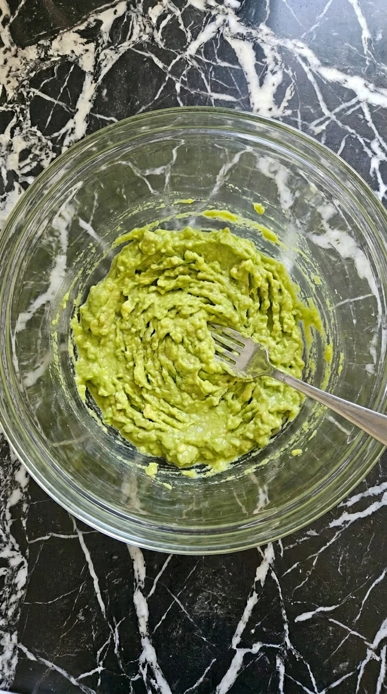 Mashing ripe avocados in a glass bowl with a fork