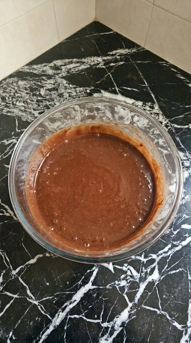 Glossy mahogany chocolate cupcake batter being mixed in a clear glass bowl