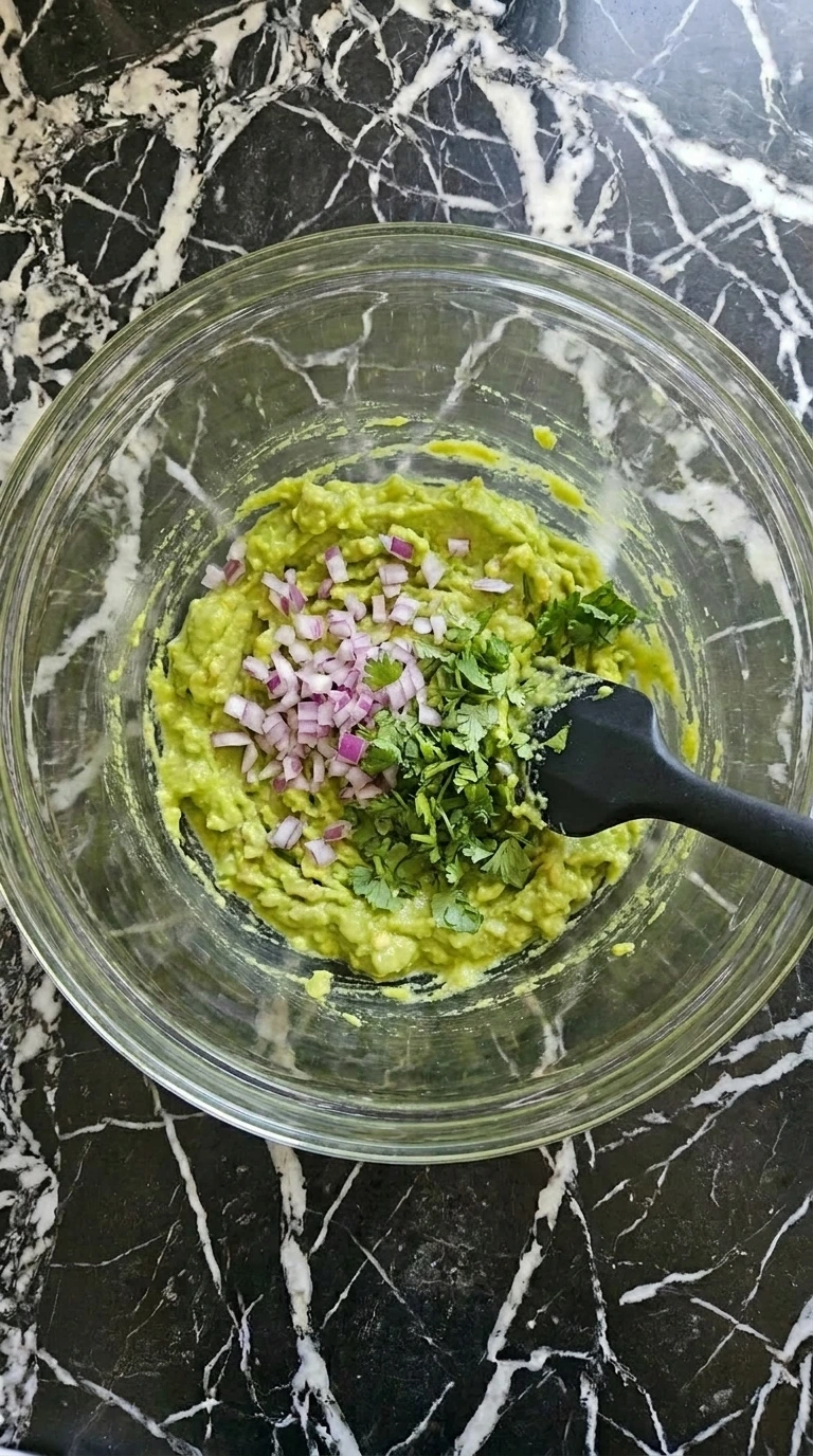 Mixing onion cilantro and lime into mashed avocado