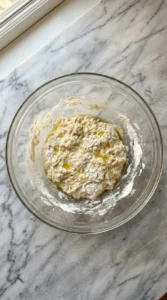 Mixing raw flour water and yeast in a glass bowl to form a shaggy pizza dough