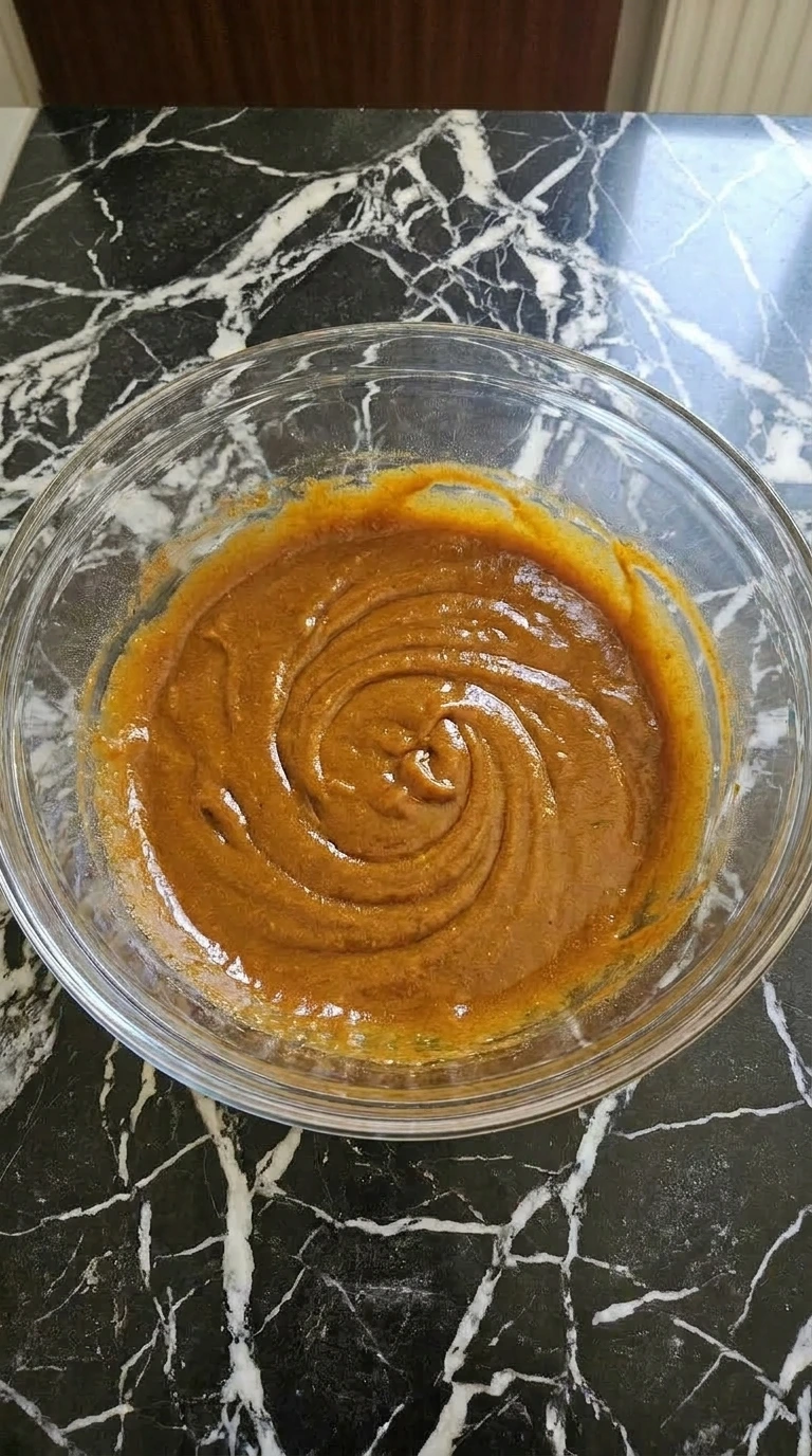 Glossy orange wet batter mixture containing pumpkin puree sugars oil and eggs in a glass bowl