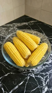 Raw corn cobs coated in oil and salt in a glass bowl