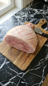 Scoring a raw ham with diamond patterns on a wooden board.