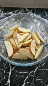 Seasoned raw potato wedges glistening with olive oil and spices in a glass bowl