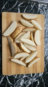 Raw russet potato wedges cut into 1/2-inch pieces on a wooden cutting board