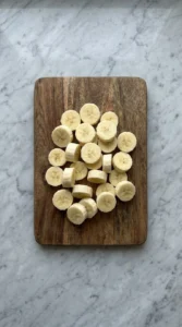 Fresh banana rounds sliced on a wooden cutting board.