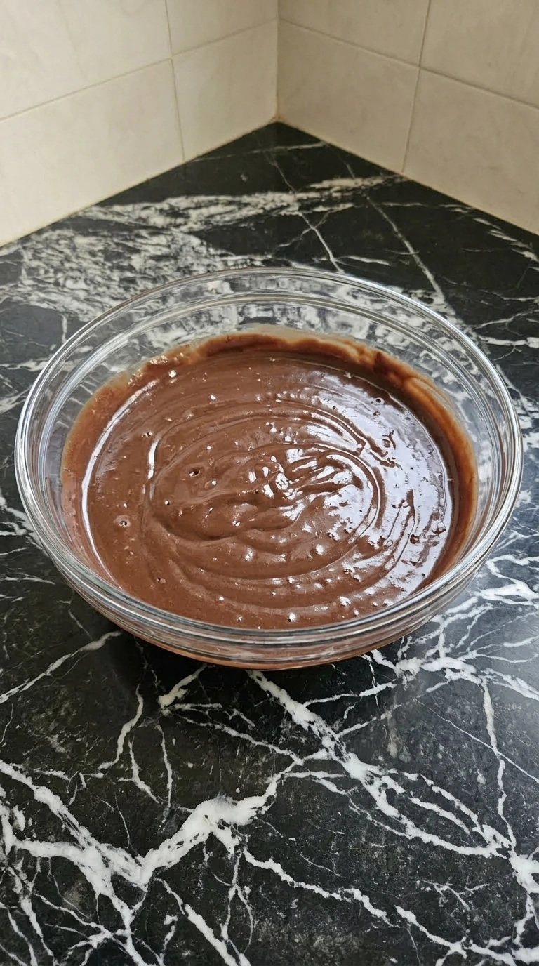 Smooth deep brown chocolate pudding filling a large glass bowl after being whisked.