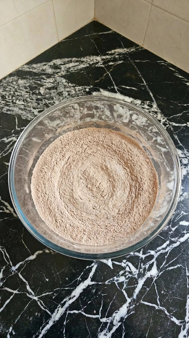Sifted pale brown flour and cocoa powder mixture inside a large clear glass mixing bowl