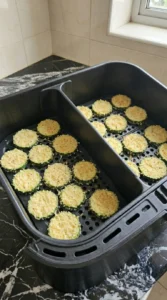 Breaded zucchini coins turning pale gold in an air fryer basket Recipe focus: Air Fryer Zucchini And Parmesan.