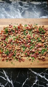 Crumbled bacon, chopped pecans, and minced parsley spread out on a wooden cutting board.