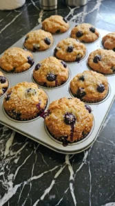 Golden brown baked blueberry muffins inside a metal tin freshly removed from the oven