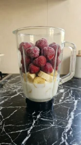 Ingredients layered inside a clear blender jar with milk at the bottom and strawberries on top
