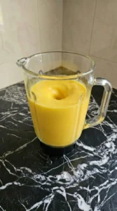 Vibrant yellow mango smoothie blending inside a clear glass jar