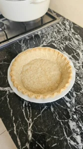 Par-baked empty pie crust with crimped edges in a white dish