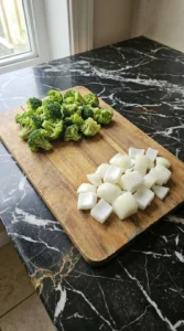 Freshly chopped green broccoli florets and diced white onion on a wooden board