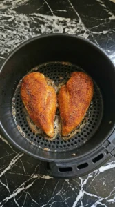 Chicken breasts cooking inside a black air fryer basket