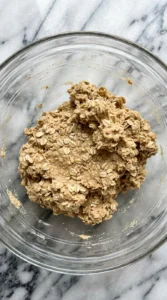 Thick textured oatmeal cookie dough fully mixed in a glass bowl.