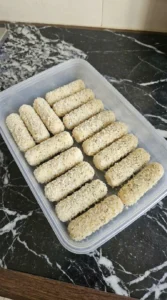 Frozen breaded cheese sticks spaced out inside a plastic storage container before baking.