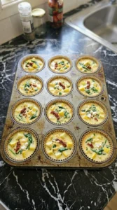 Twelve muffin cups filled with patty pan squash egg mixture before baking.