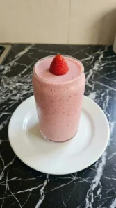 A clear glass tumbler filled with pink strawberry smoothie and garnished with a fresh berry